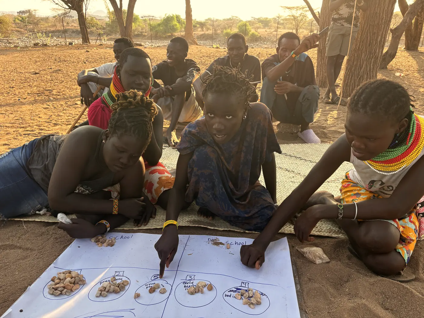 Women place stones on a paper chart to show how many girls in their community are in school.